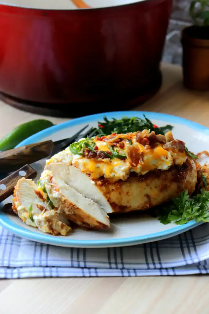 side view of creamy cheesy dutch oven jalapeno popper recipe on a white plate and blue rim.