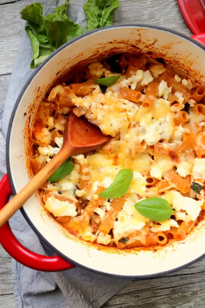 One pot baked ziti being served from a Dutch oven with layers of pasta and cheese.