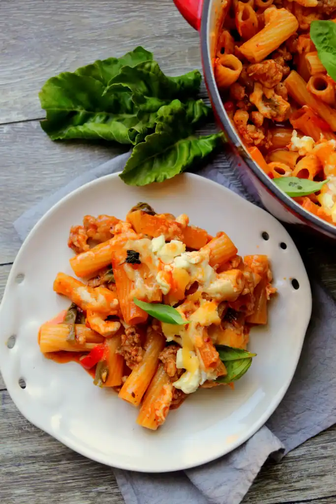 Close up of cheesy baked ziti in a Dutch oven, topped with fresh basil.