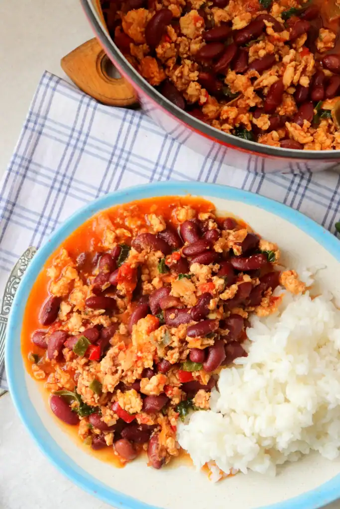 a bowl of cooked white rice with homemade dutch oven chili on a white plate with a blue rim