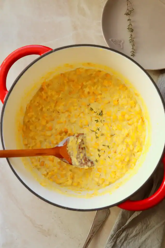 Dutch oven filled with creamy corn topped with melted butter and cracked pepper.