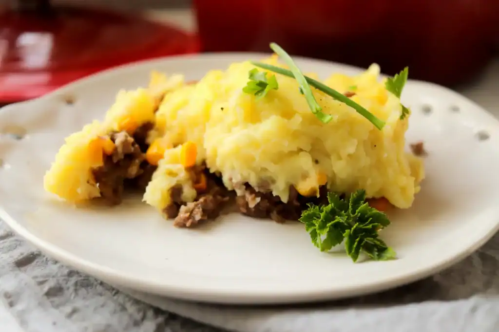 Slice of shepherd’s pie scooped from a Dutch oven, showing layers of meat and potatoes.