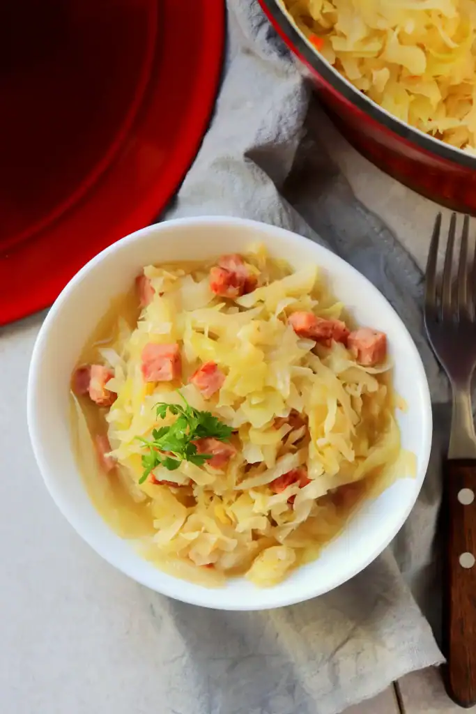 Close-up of smothered cabbage cooked in a Dutch oven with andouille sausage and seasoning.