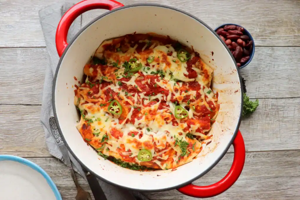 A serving of vegetarian enchiladas scooped from a Dutch oven with gooey cheese and sauce.